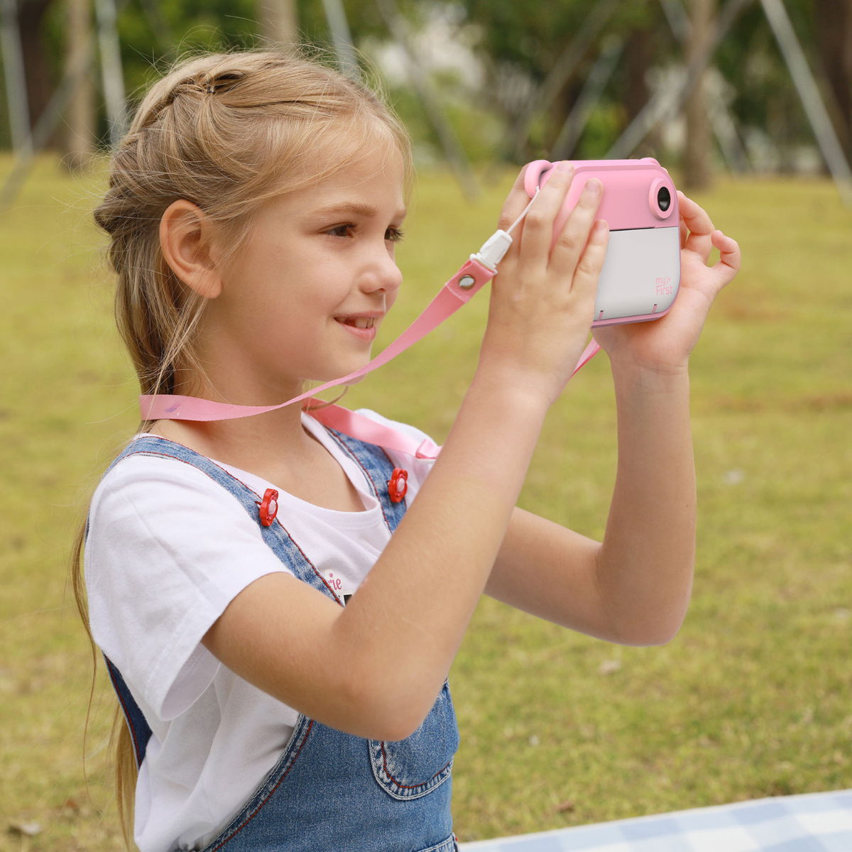 Young girl holding a pink camera in a grassy outdoor setting - myFirst Insta 2 Pink